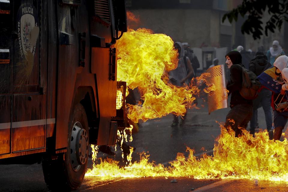 An anti-government protester wearing a Guy Fawkes mask stands with a shield near flames from molotov cocktails thrown at a water cannon by anti-government protesters during riots in Caracas in this April 20, 2014 file photo. To match Insight VENEZUELA-INFORMERS/ REUTERS/Jorge Silva/Files