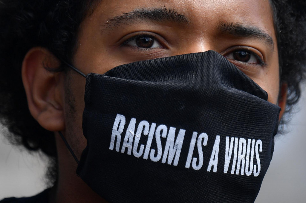 A protester wears a protective face covering with the slogan ”Racism is a Virus” written on the fabric as he listens to speeches at a gathering in support of the Black Lives Matter movement at Marble Arch in London on July 5, 2020, in the aftermath of the death of unarmed black man George Floyd in police custody in the US. (Photo by JUSTIN TALLIS/AFP)