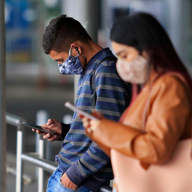 People wear face masks as they check their mobile phones outside El Dorado International Airport in Bogota on August 14, 2020, amid the new coronavirus pandemic. - Bogota&amp;#39;s Mayor Claudia Lopez authorized some passenger flights at El Dorado International Airport and will allow restaurants with outdoor seating to reopen from September 1. (Photo by DANIEL MUNOZ/AFP)
