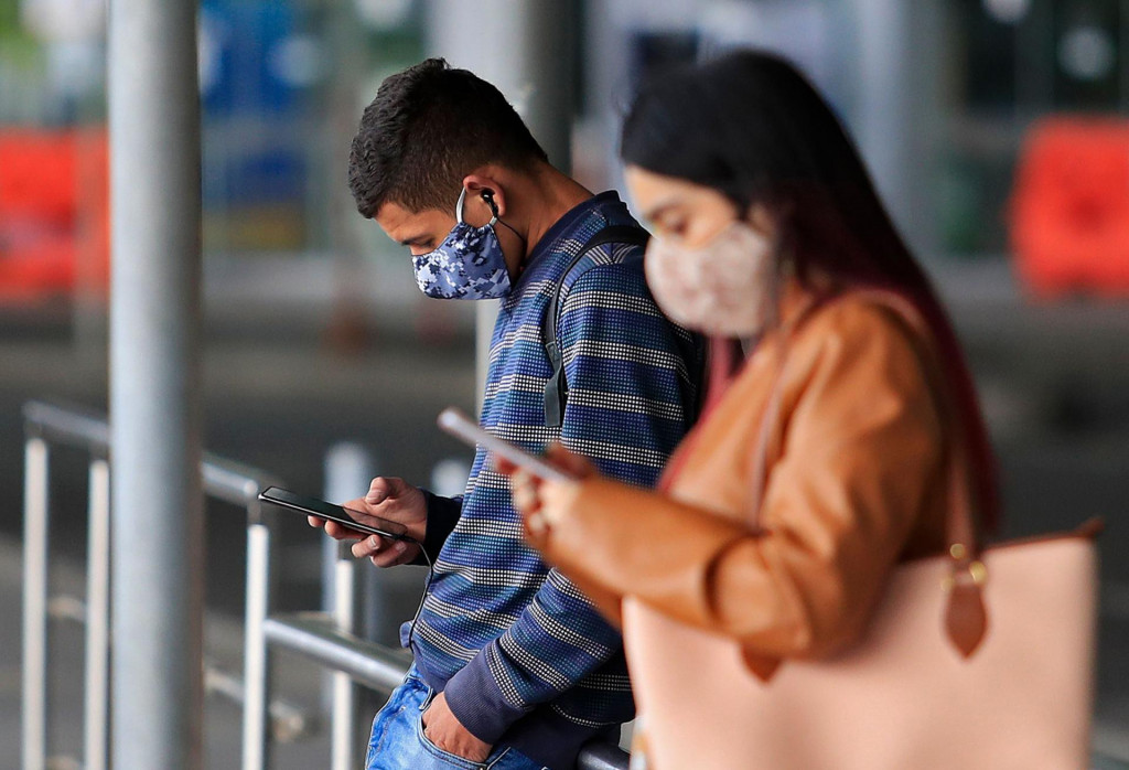 People wear face masks as they check their mobile phones outside El Dorado International Airport in Bogota on August 14, 2020, amid the new coronavirus pandemic. - Bogota&amp;#39;s Mayor Claudia Lopez authorized some passenger flights at El Dorado International Airport and will allow restaurants with outdoor seating to reopen from September 1. (Photo by DANIEL MUNOZ/AFP)