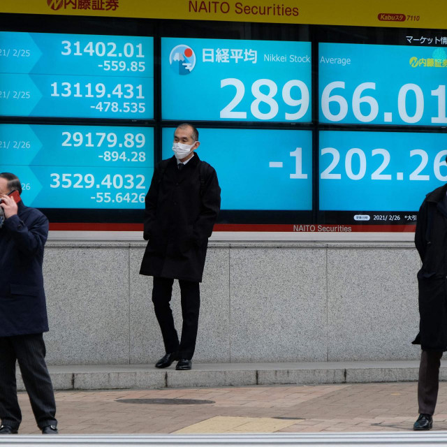 Pedestrians stand in front of an electronic quotation board displaying the closing numbers of share prices on the Tokyo Stock Exchange in Tokyo on February 26, 2021. (Photo by Kazuhiro NOGI/AFP)