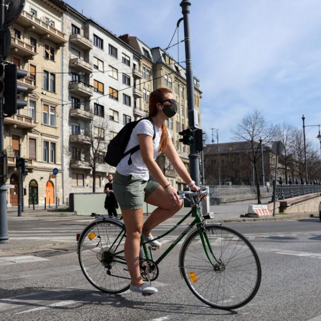 Mlada žena sa zaštitnom maskom vozi bicikl ulicama Budimpešte.