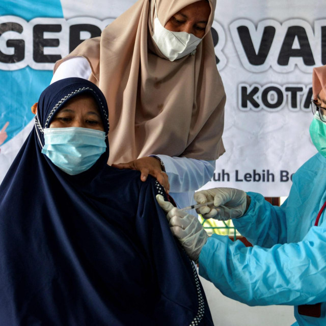 A woman (L) receives the Sinovac vaccine against the Covid-19 coronavirus during a vaccination drive at a community centre in Banda Aceh on June 28, 2021. (Photo by CHAIDEER MAHYUDDIN/AFP)