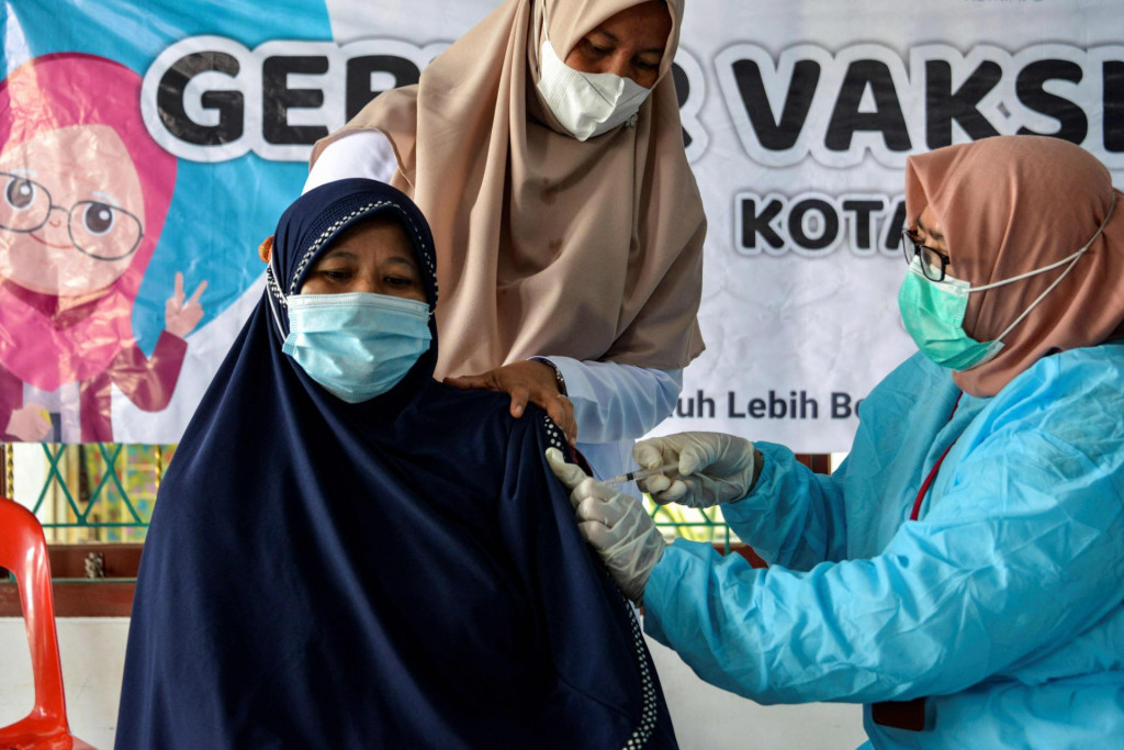 A woman (L) receives the Sinovac vaccine against the Covid-19 coronavirus during a vaccination drive at a community centre in Banda Aceh on June 28, 2021. (Photo by CHAIDEER MAHYUDDIN/AFP)