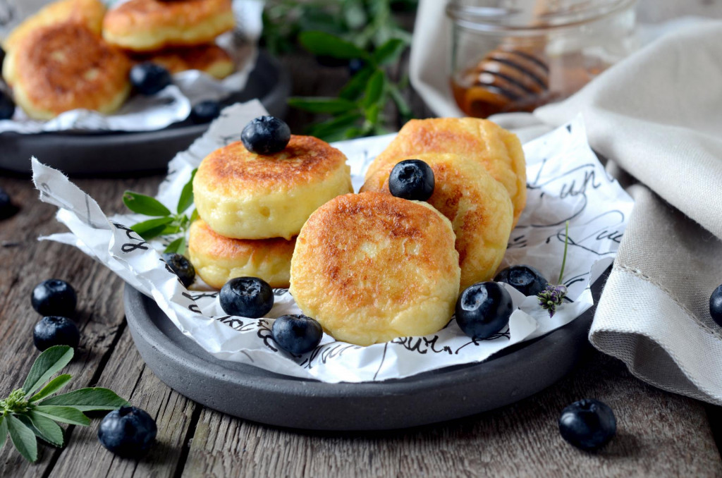 cheese pancakes with blueberries, blackberries and honey on a wooden table