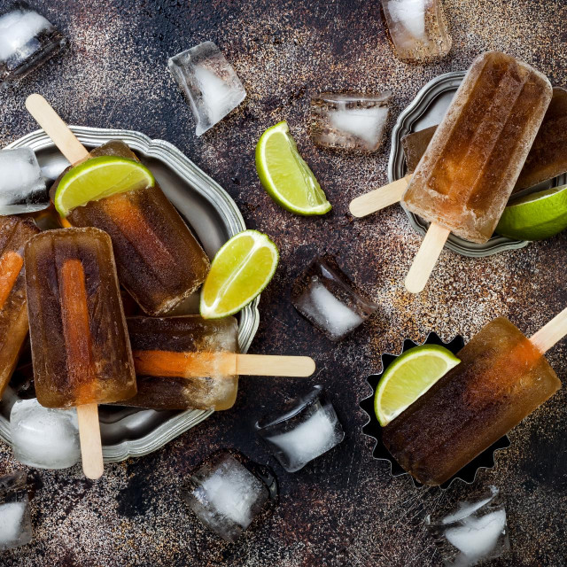 Rum and coke cocktail popsicles with lime juice. Cuba libre homemade frozen alcoholic paletas - ice pops. Overhead, flat lay, top view, copy space
