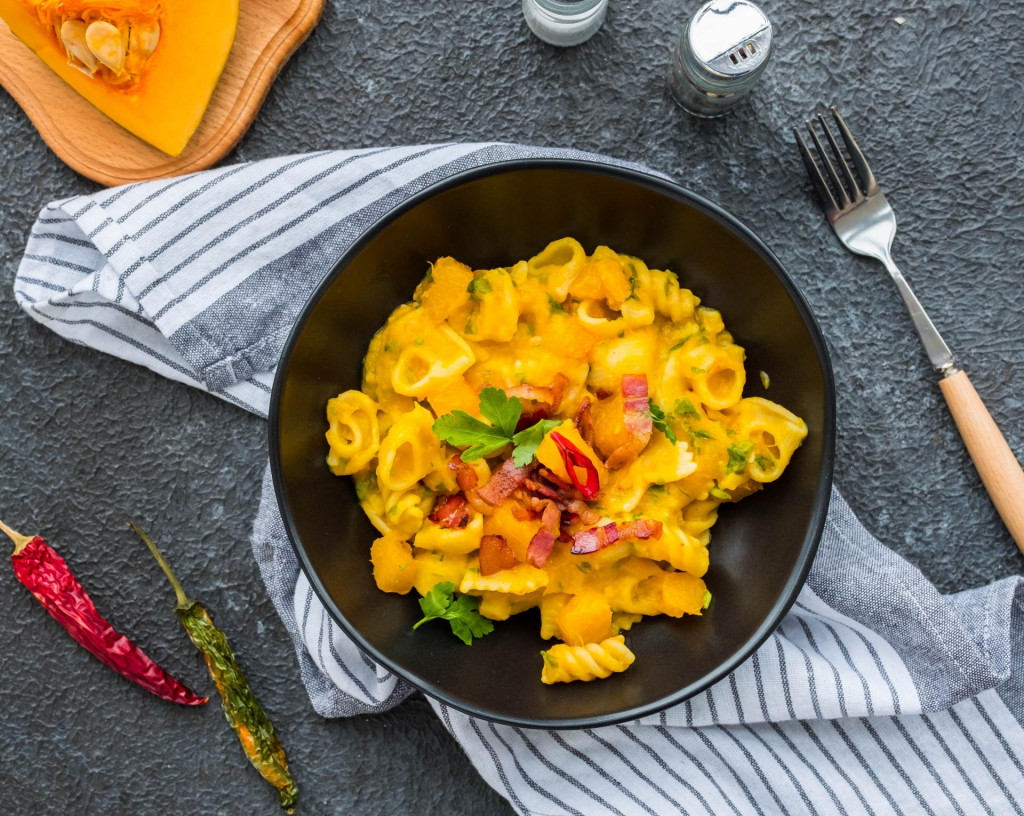 Pasta with pumpkin, fried bacon and hot peppers in a black plate on a dark concrete background. Pasta recipes. Italian food.