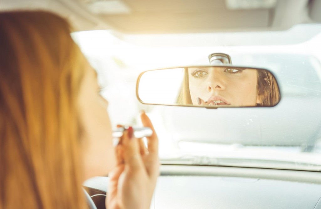 woman putting lipstick in the car. she watch herself in the mirror while she is driving