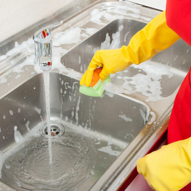 Person hands in yellow gloves cleaning the kitchen sink with disinfectant