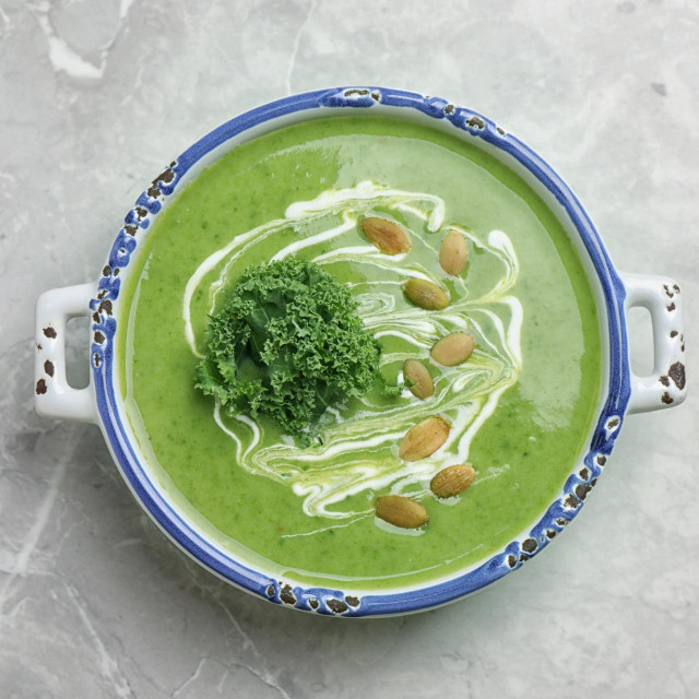 Tasty kale soup with pumpkin seeds on light grey marble table, top view