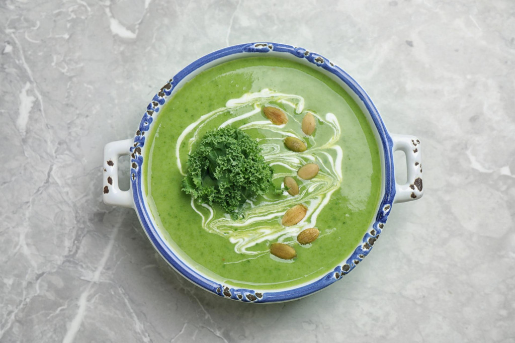 Tasty kale soup with pumpkin seeds on light grey marble table, top view