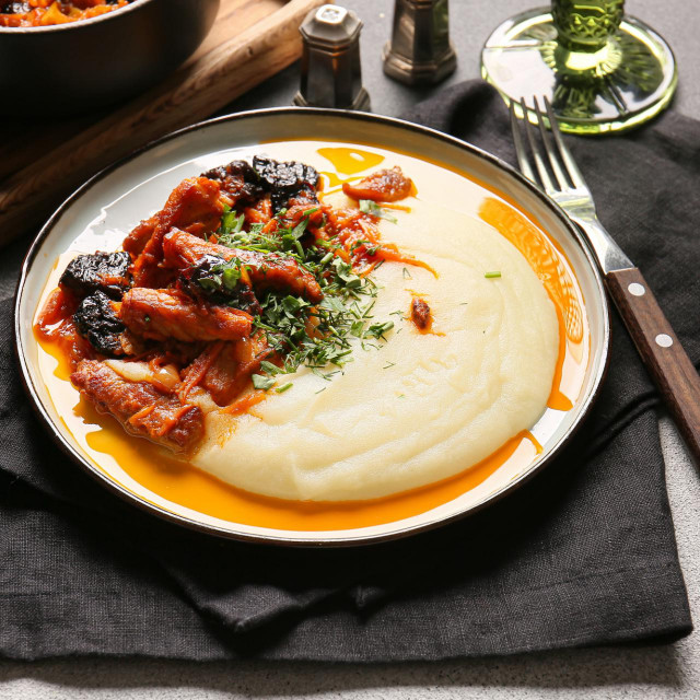 Plate with delicious mashed potatoes, gravy and beef stew with prunes on dark table�