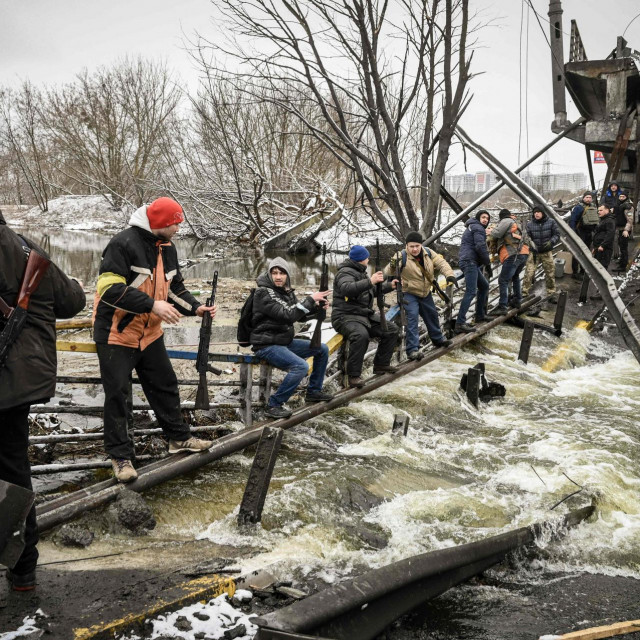 Pripadnici ukrajinske civilne zaštite prenose puške ispod jednog od srušenih mostova