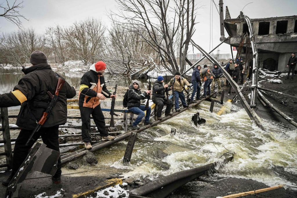 Pripadnici ukrajinske civilne zaštite prenose puške ispod jednog od srušenih mostova