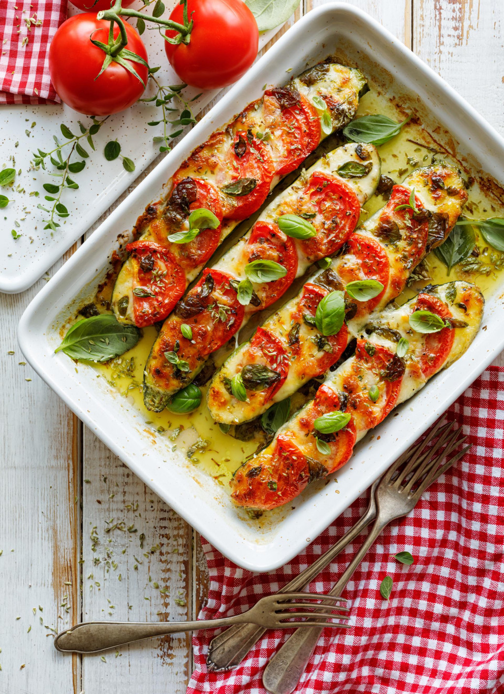 Roasted, stuffed zucchini with the addition of tomatoes, mozzarella cheese, fresh basil and olive oil (caprese salad) in a ceramic baking dish, close-up, top view. Nutritious and tasty vegetarian dish