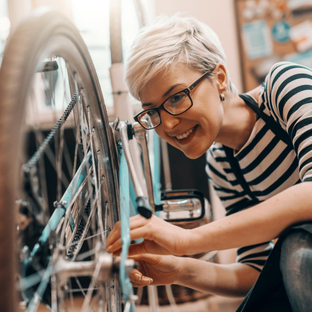 &lt;p&gt;Beautiful Caucasian female worker with short blonde hair and eyeglasses crouching and repairing bicycle. Bike workshop interior.&lt;/p&gt;