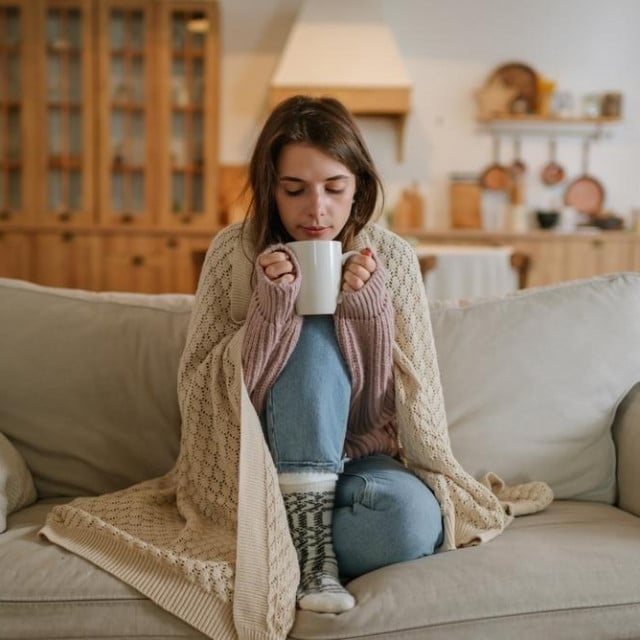 &lt;p&gt;Woman freezes in winter time. Young girl wearing warm woolen socks and wrapped into plaid, holding a cup of hot drink while sitting on sofa at home. Keep warm.&lt;/p&gt;