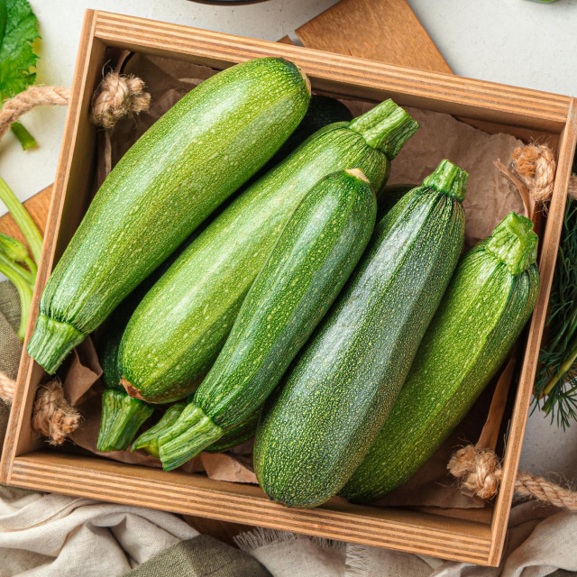 Slicing zucchini on a cutting board. Ripe zucchini on a gray background. Top view, horizontal.