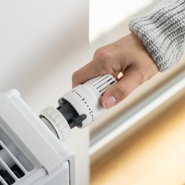 &lt;p&gt;A woman in a warm sweater turns the regulator of the thermostatic radiator valve to the middle position to set the economical heating mode of the room. Heating of the apartment in the cold season.&lt;/p&gt;