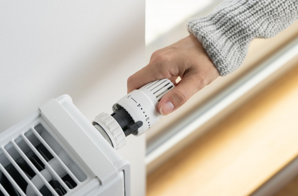 &lt;p&gt;A woman in a warm sweater turns the regulator of the thermostatic radiator valve to the middle position to set the economical heating mode of the room. Heating of the apartment in the cold season.&lt;/p&gt;