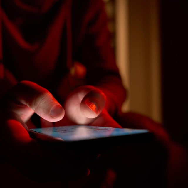<p>Man using smartphone at night. Close up of hand holding smartphone, swiping and scrolling social media feed on glowing screen in dark room</p>