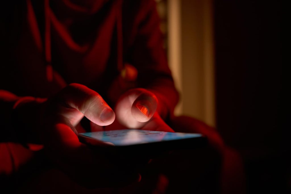 <p>Man using smartphone at night. Close up of hand holding smartphone, swiping and scrolling social media feed on glowing screen in dark room</p>