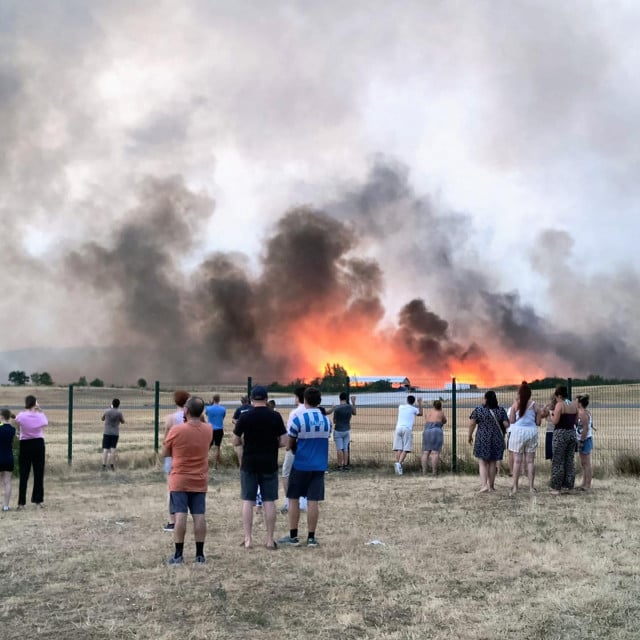 <p>TOPSHOT - Bystanders look on as fire and smoke billow across Castres-Mazamet aerodrome, near Labruguiere in south-western France on July 24, 2026. France and Spain evacuated more than 160,000 people as unprecedented forest fires ravaged areas on July 25, 2026, near Madrid and Bordeaux, a French city flanked by tourist havens and world-renowned vineyards. French President Emmanuel Macron asked the army to mobilise to help contain the worst wildfire the country has ever seen after seeking European Union help, as a local official warned the blaze was heading towards Bordeaux. (Photo by Daniel ABELOUS/AFP)</p>