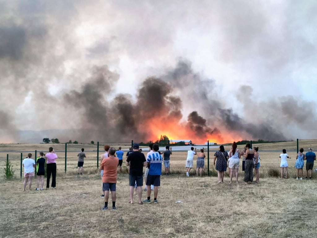 <p>TOPSHOT - Bystanders look on as fire and smoke billow across Castres-Mazamet aerodrome, near Labruguiere in south-western France on July 24, 2026. France and Spain evacuated more than 160,000 people as unprecedented forest fires ravaged areas on July 25, 2026, near Madrid and Bordeaux, a French city flanked by tourist havens and world-renowned vineyards. French President Emmanuel Macron asked the army to mobilise to help contain the worst wildfire the country has ever seen after seeking European Union help, as a local official warned the blaze was heading towards Bordeaux. (Photo by Daniel ABELOUS/AFP)</p>