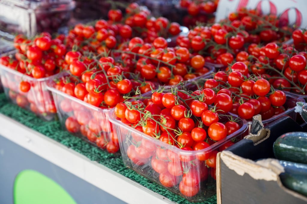 <p>Red cherry tomatoes in plastic trays, outdoor farm market</p>