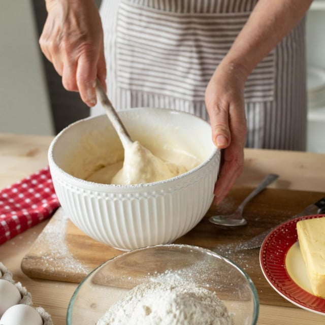 <p>Woman mixing dough or batter with a wooden spoon in a bowl for making a cake</p>